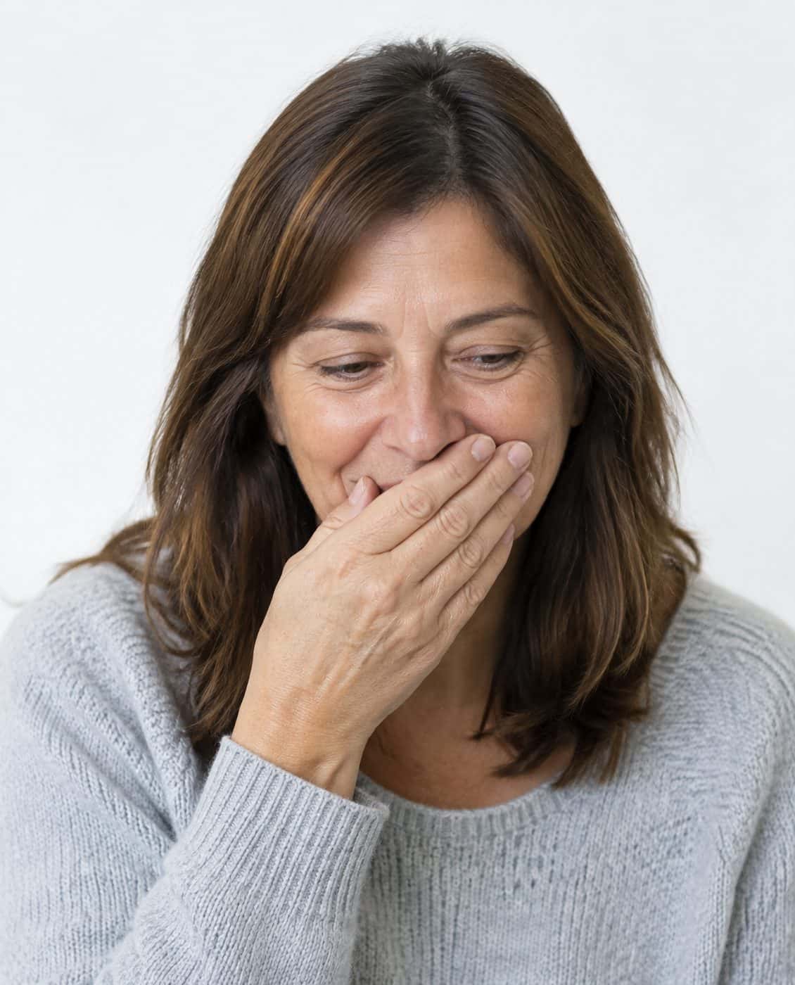 Mujer de mediana edad que pasa de taparse la boca a sonreír con confianza